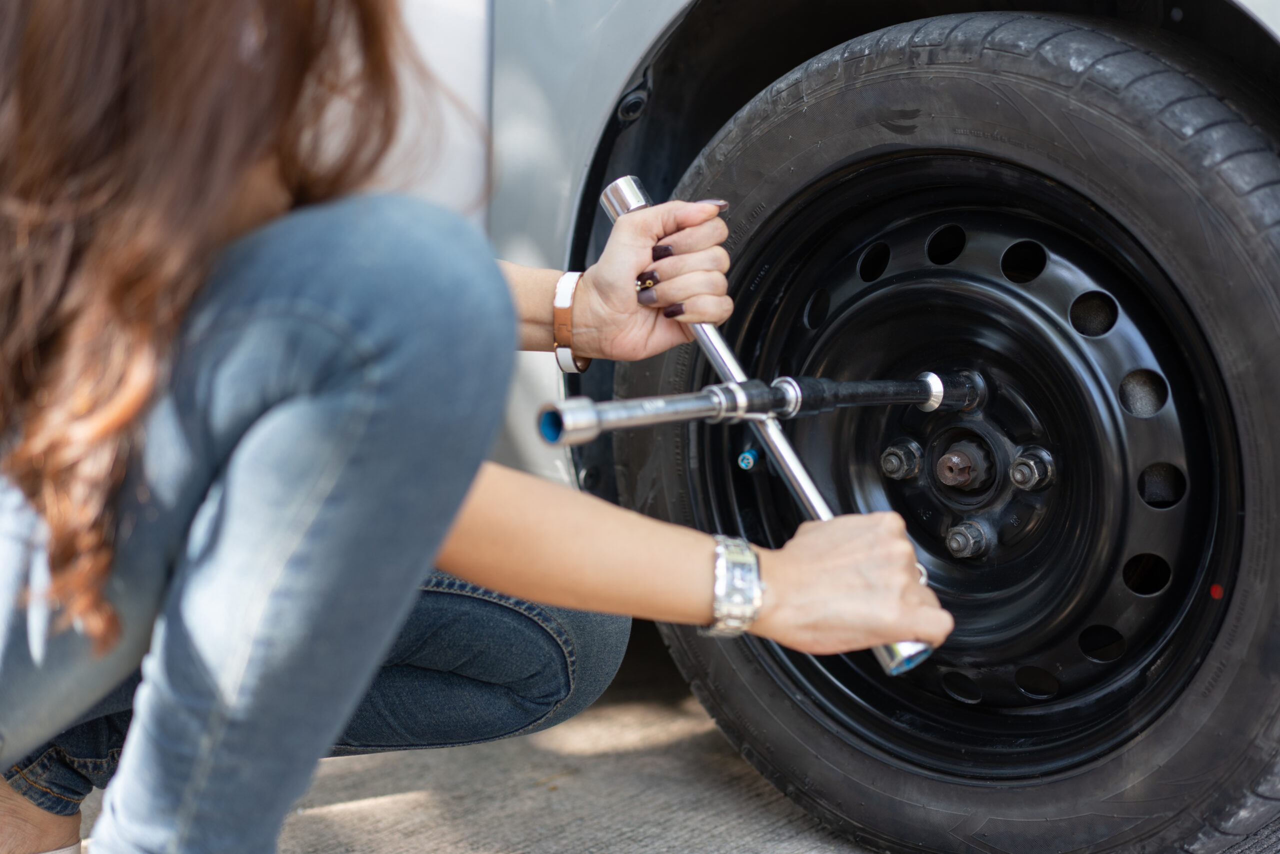 Smart and Attractive Asian woman jacks up her car and uses a wrench to change the wheel on a broken car, uses tools or equipment, tries to solve problems by self, Car Repairing and insurance concept